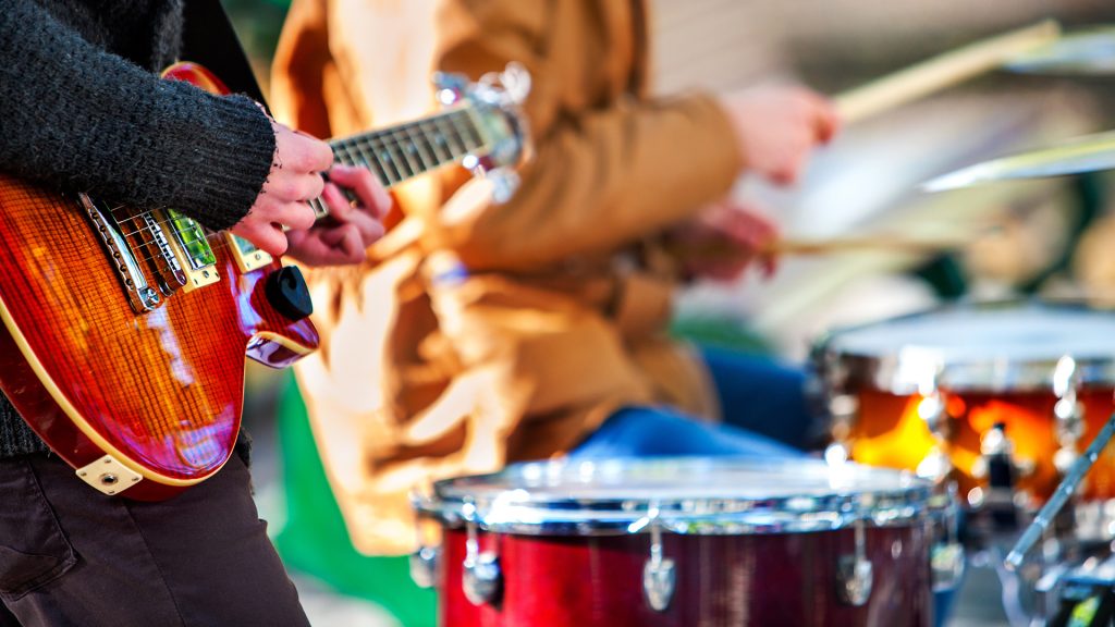 Festival music band. Hands playing on percussion instruments in city park . Drums with sticks closeup. Body part of male musicians. Sharpen is guitar and man hand.